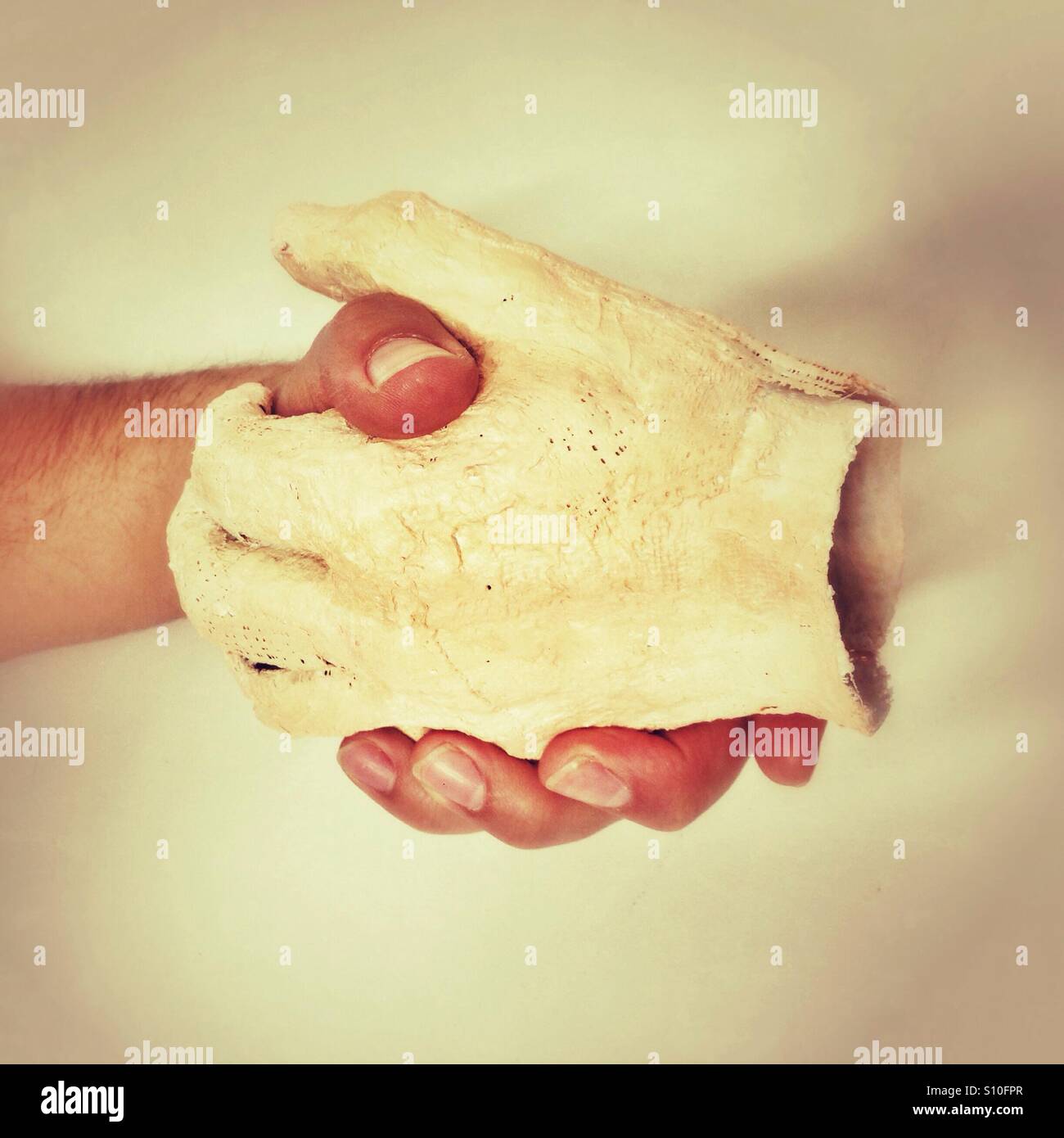 Handmade plaster cast representing a human hand is held gently by another hand in an intimate moment of connection and support - Smartphone Captured Stock Image