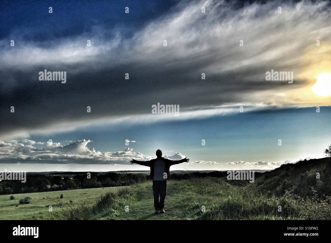 Man with outstretched arms under unusual cloud formation in Dorset landscape - Smartphone Captured Stock Image