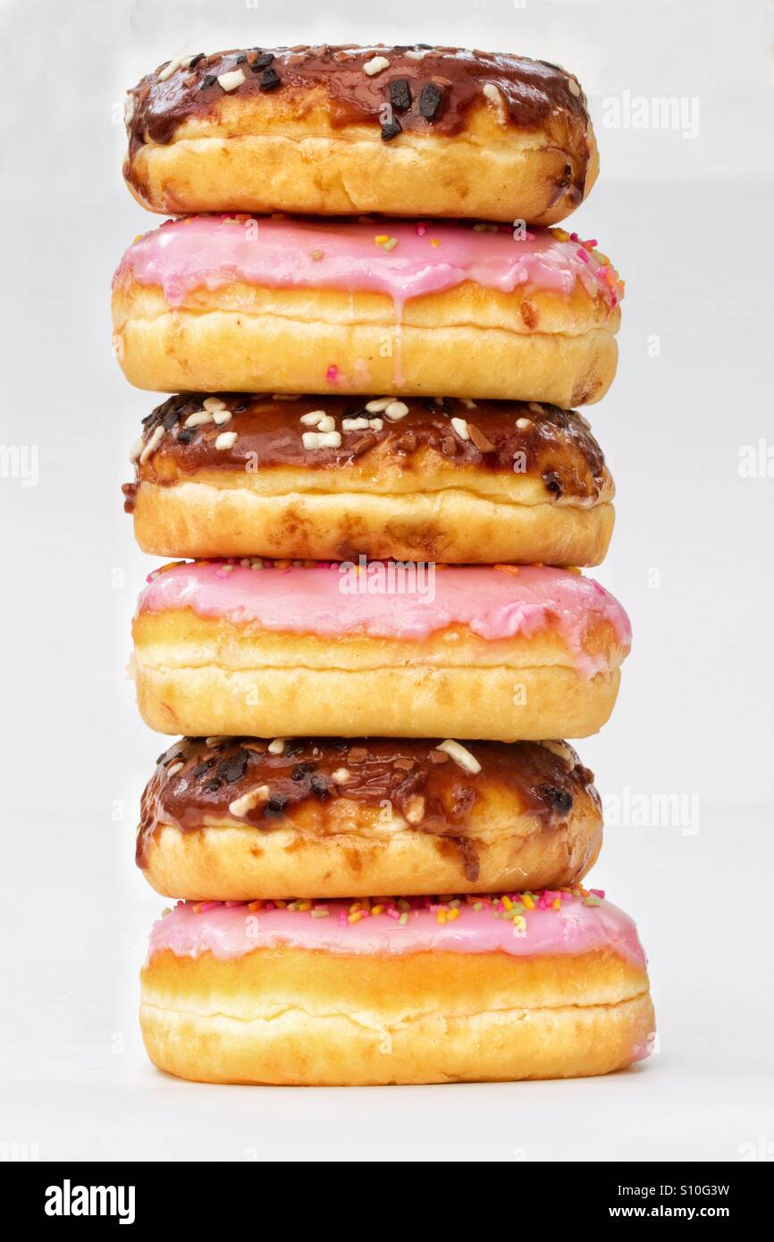 A tall stack of doughnuts with chocolate and pink icing on an isolated white background. Stock Photo