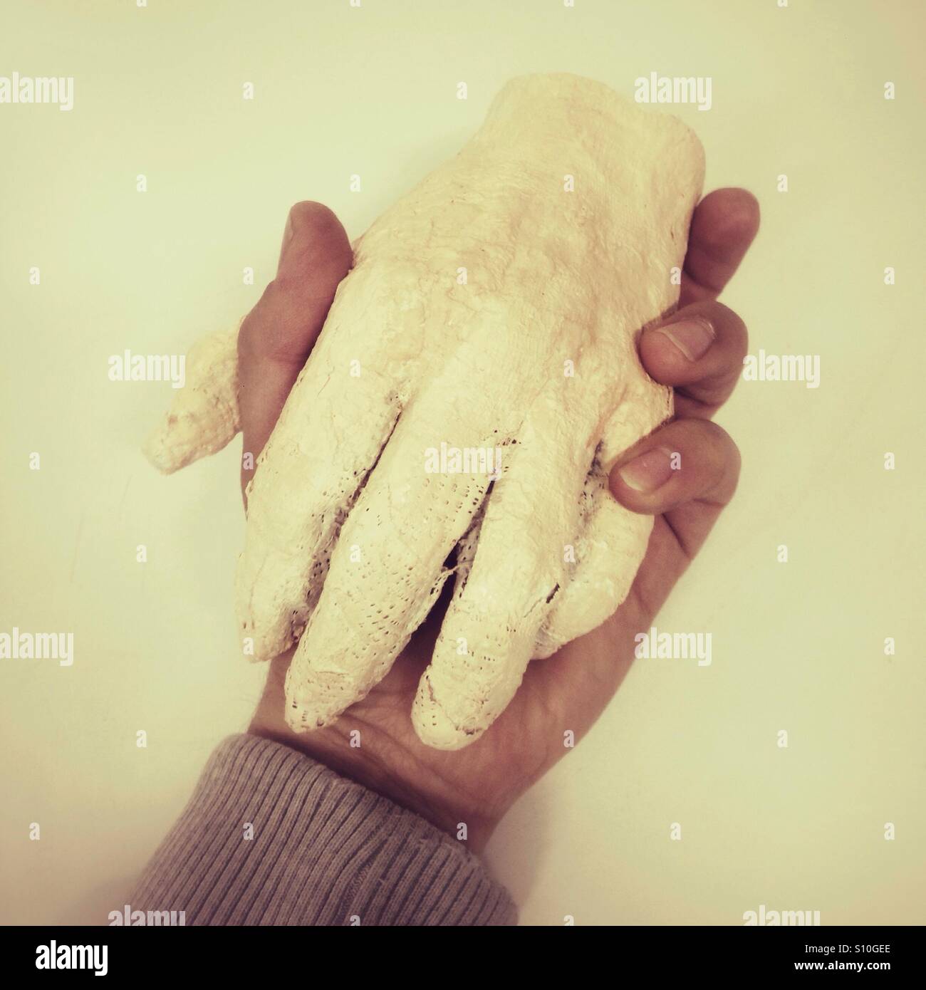 Handmade plaster cast representing a human hand is held gently by another hand in an intimate moment of connection and support - Smartphone Captured Stock Image