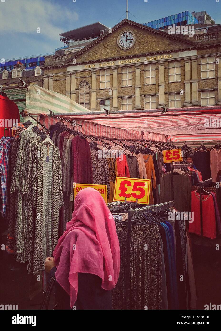 Woman in hijab passing a colourful Bangladeshi clothes stall in the Whitechapel market. Royal London hospital in background.London. U.K. Stock Photo