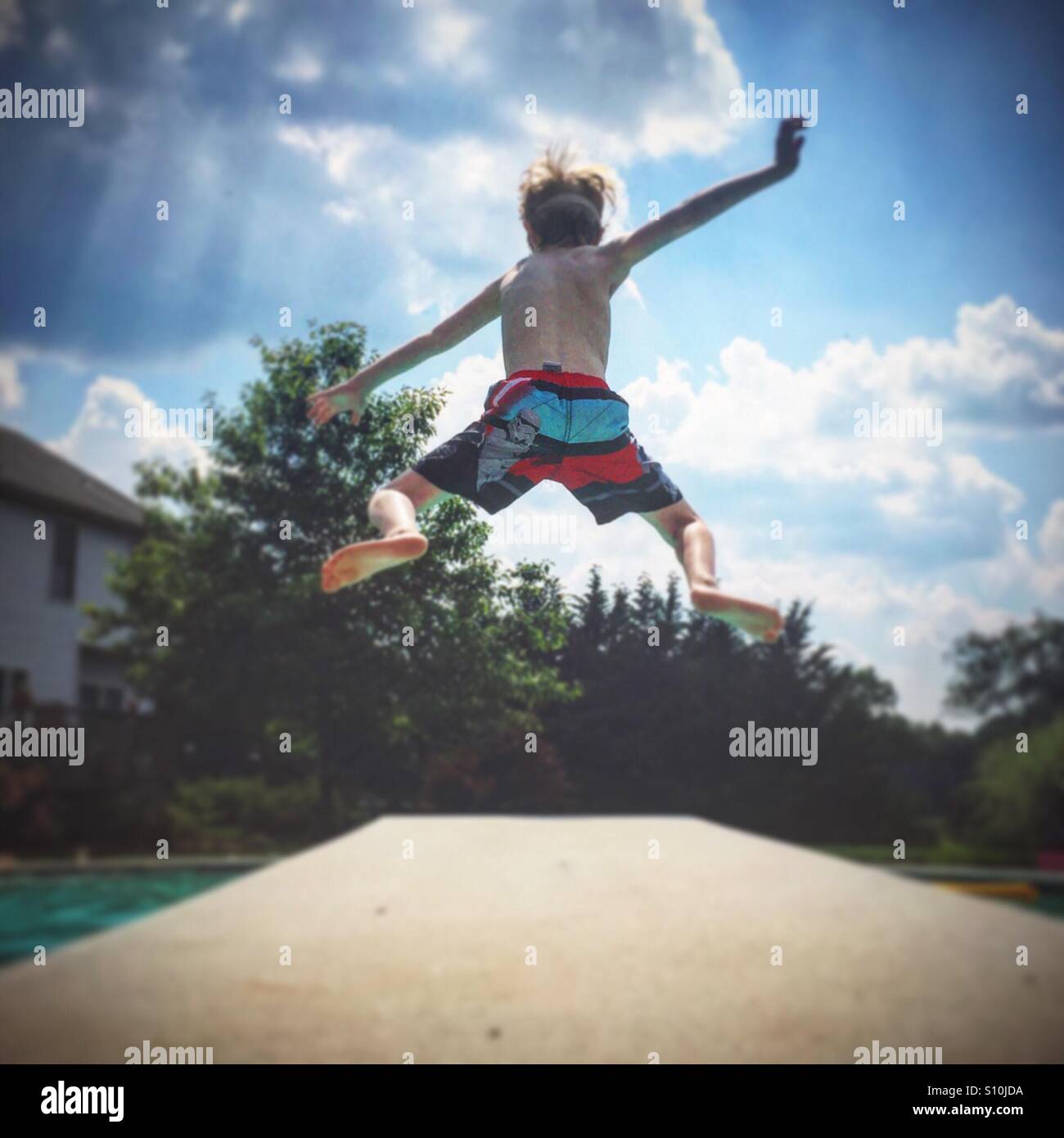 A young boy jumps off a diving board and into a swimming pool on a hot summer day Stock Photo