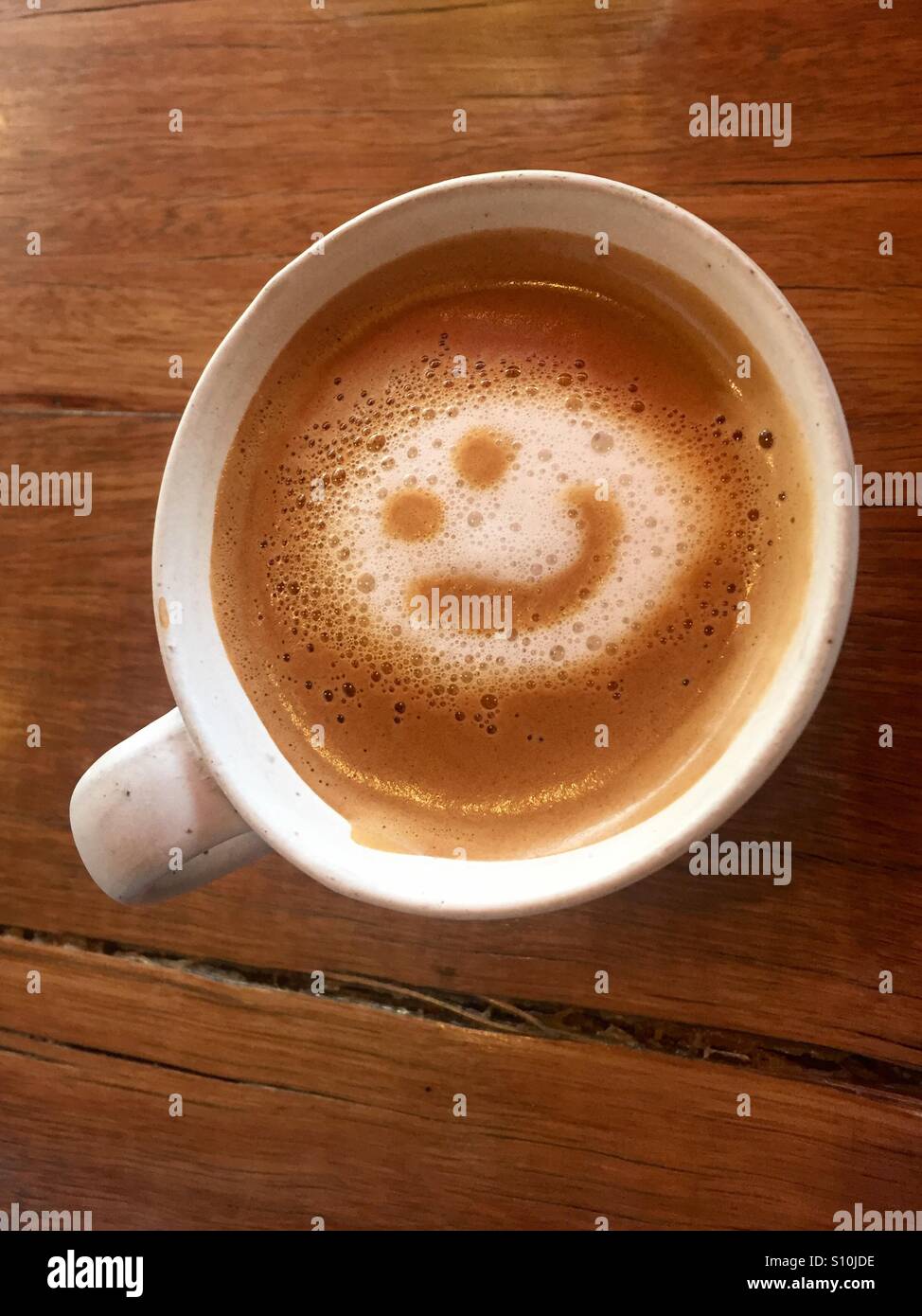 Coffee smile drawn in foam in white cup on wood table - Smartphone Captured Stock Image