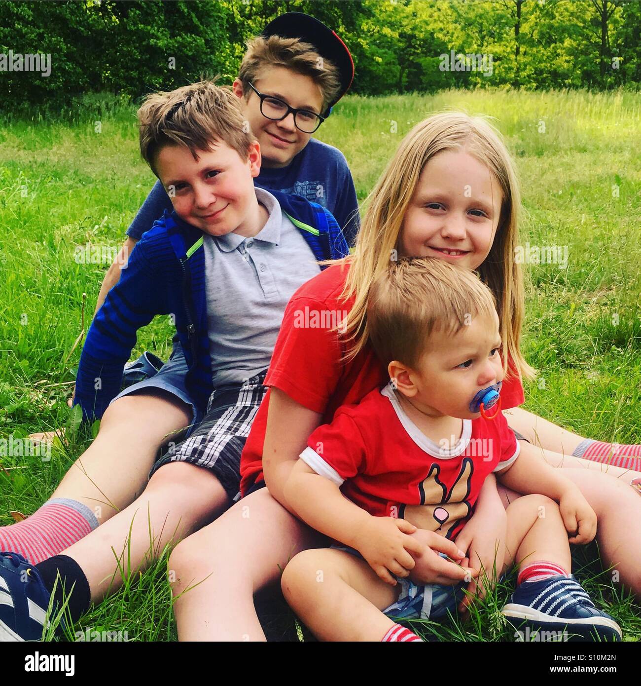 4 siblings sitting on a grass  on a hot spring day Stock Photo