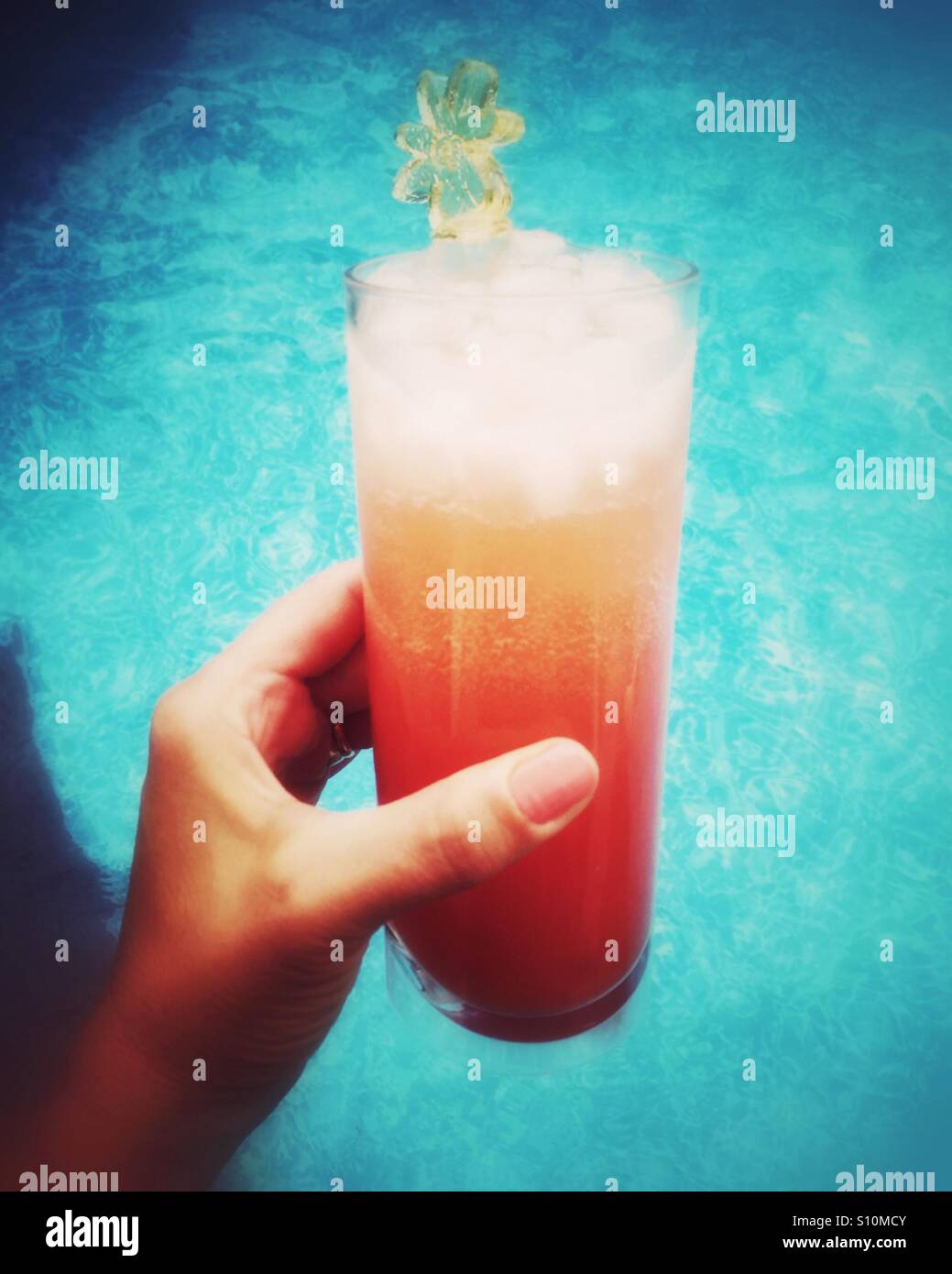 A close up of an icy beverage being held by a woman by a swimming pool. - Smartphone Captured Stock Image