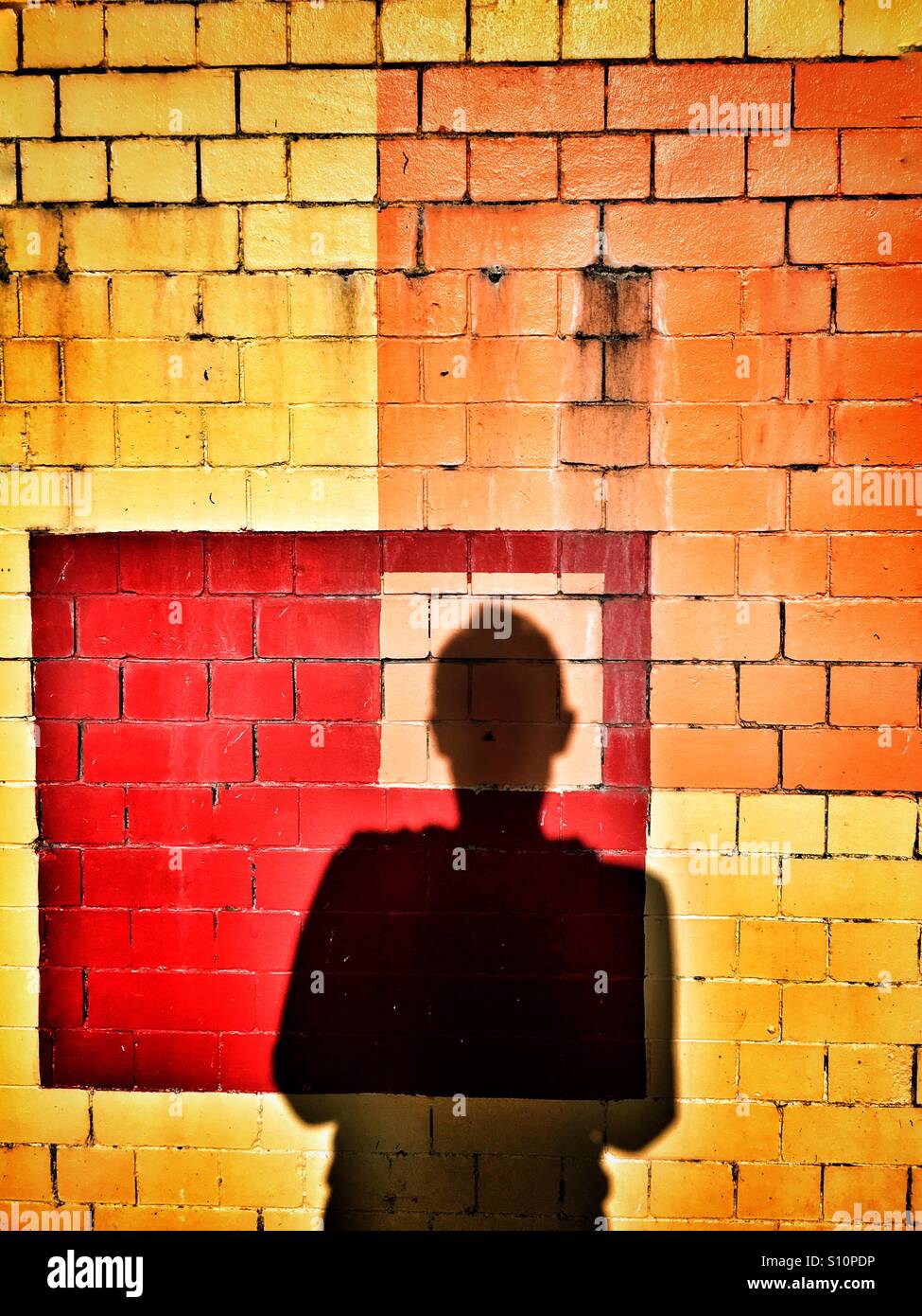 Shadow of man against abstract squares painted on brick wall Stock Photo