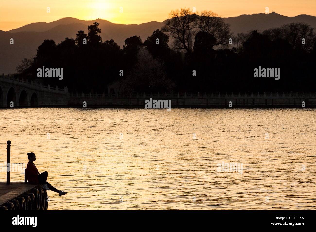 Girl sitting on the dock near the pond during sunset Stock Photo - Alamy