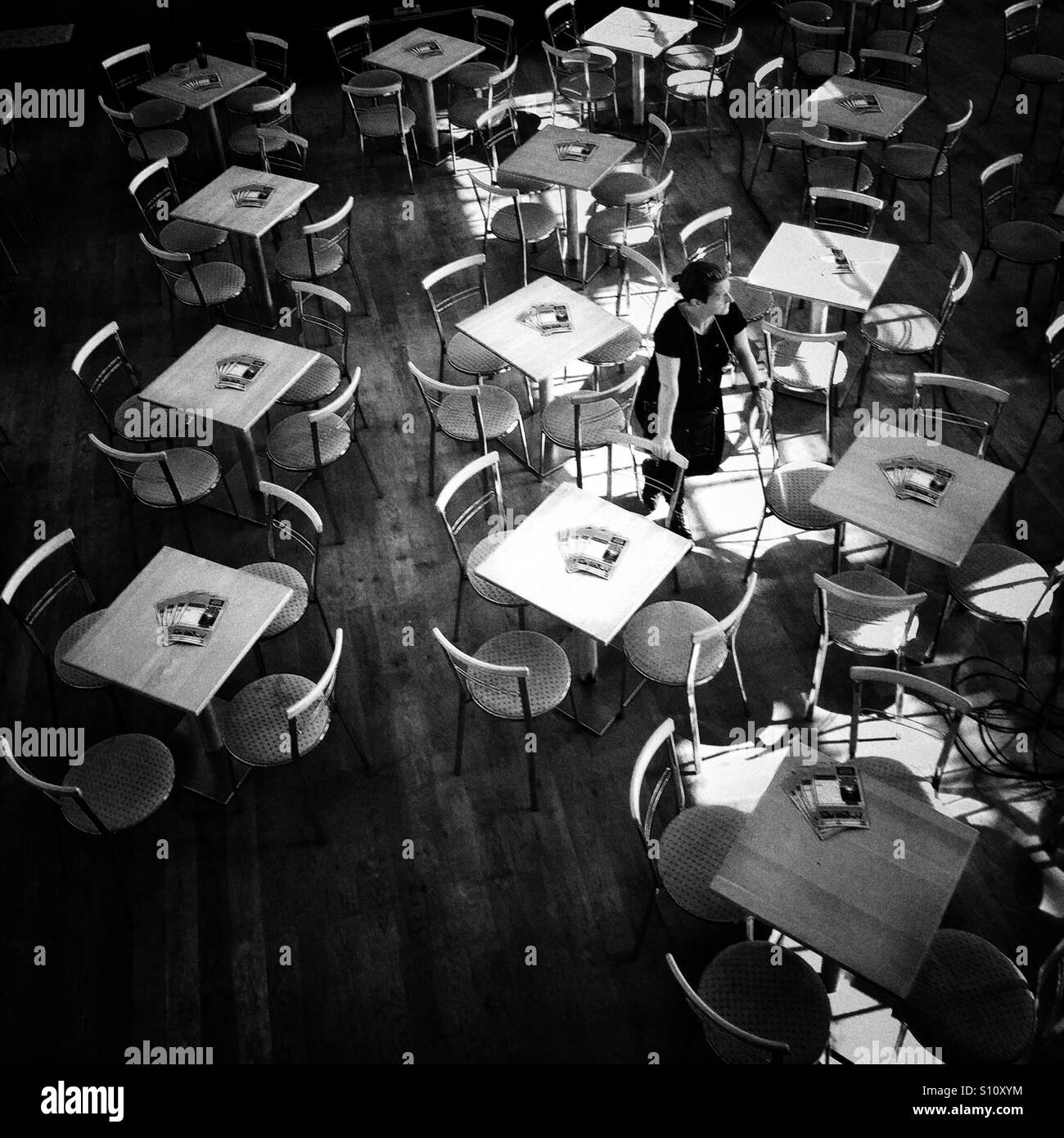 Setting up tables prior to an event. A woman stands amongst the tables in a cafe. - Smartphone Captured Stock Image