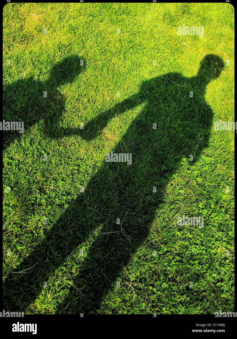 Shadows on the grass of a man and a boy, both holding hands. Is it Father and Son happy together OR is a Paedophile forcing the child away? A Social Issues & Concept Picture. Photo © COLIN HOSKINS. - Smartphone Captured Stock Image