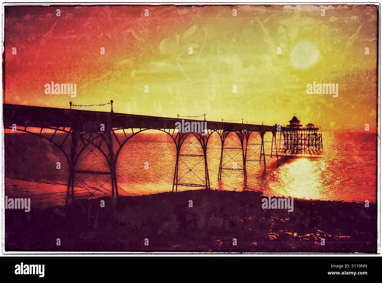 An Antique Grunge Effect Picture of the Sun Setting over Clevedon Pier in North Somerset, England. Clevedon Pier is the only visitable Grade One Listed Pier in England. Photo Credit - © COLIN HOSKINS. - Smartphone Captured Stock Image
