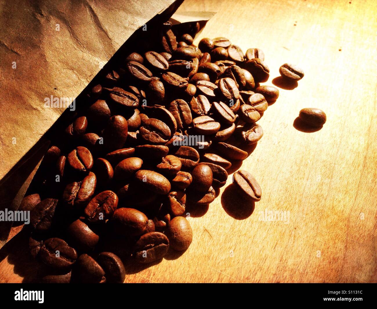 Monsoon washed arabica coffee beans spilled onto a wooden surface from a brown paper back Stock Photo