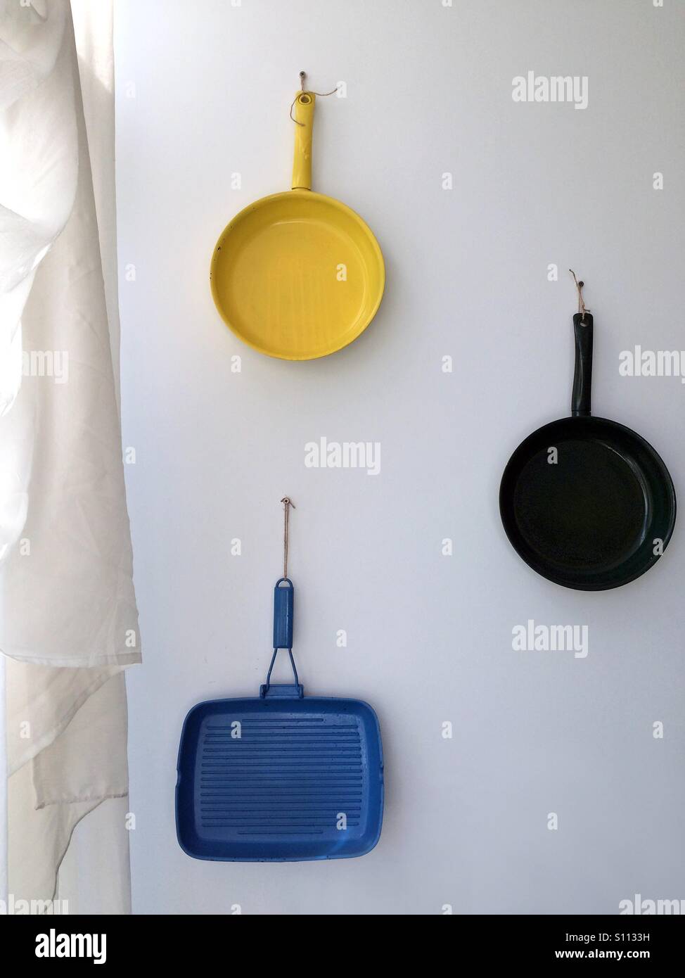 Three colored pans hanging on the wall - Smartphone Captured Stock Image