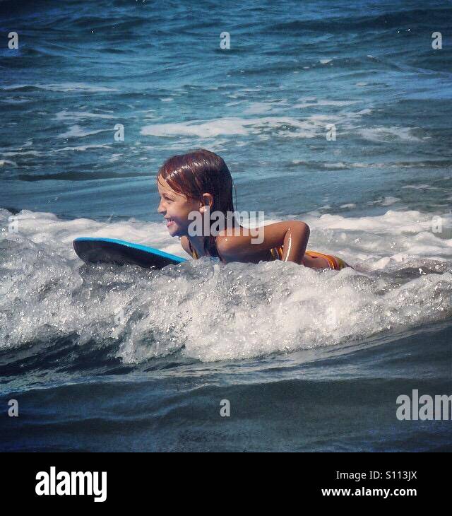 Little girl smiling while catching a wave on a boogie board in the