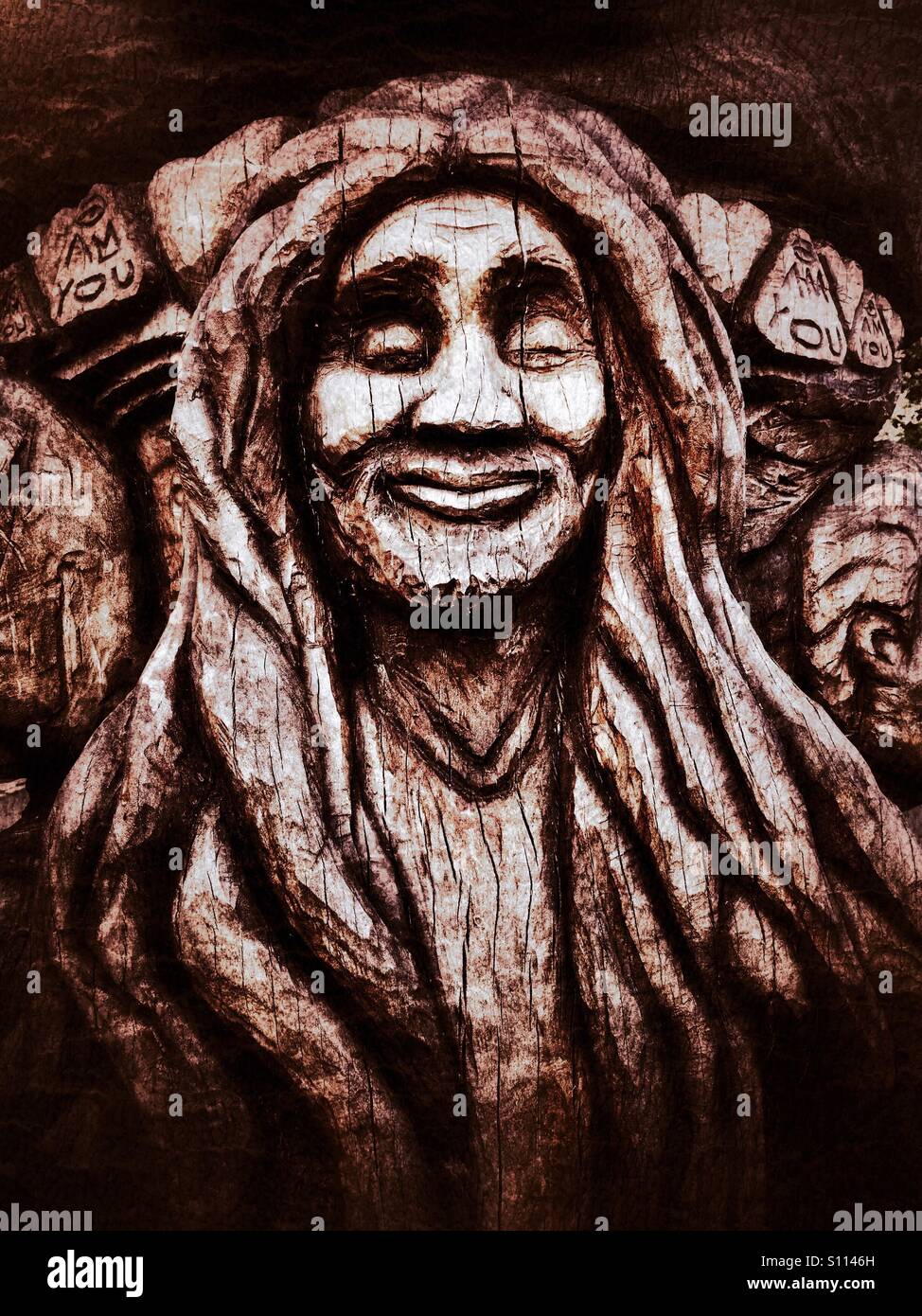 Face of tranquil smiling dreadlocked man carved into a wooden sculpture at Peckham Rye park - Smartphone Captured Stock Image