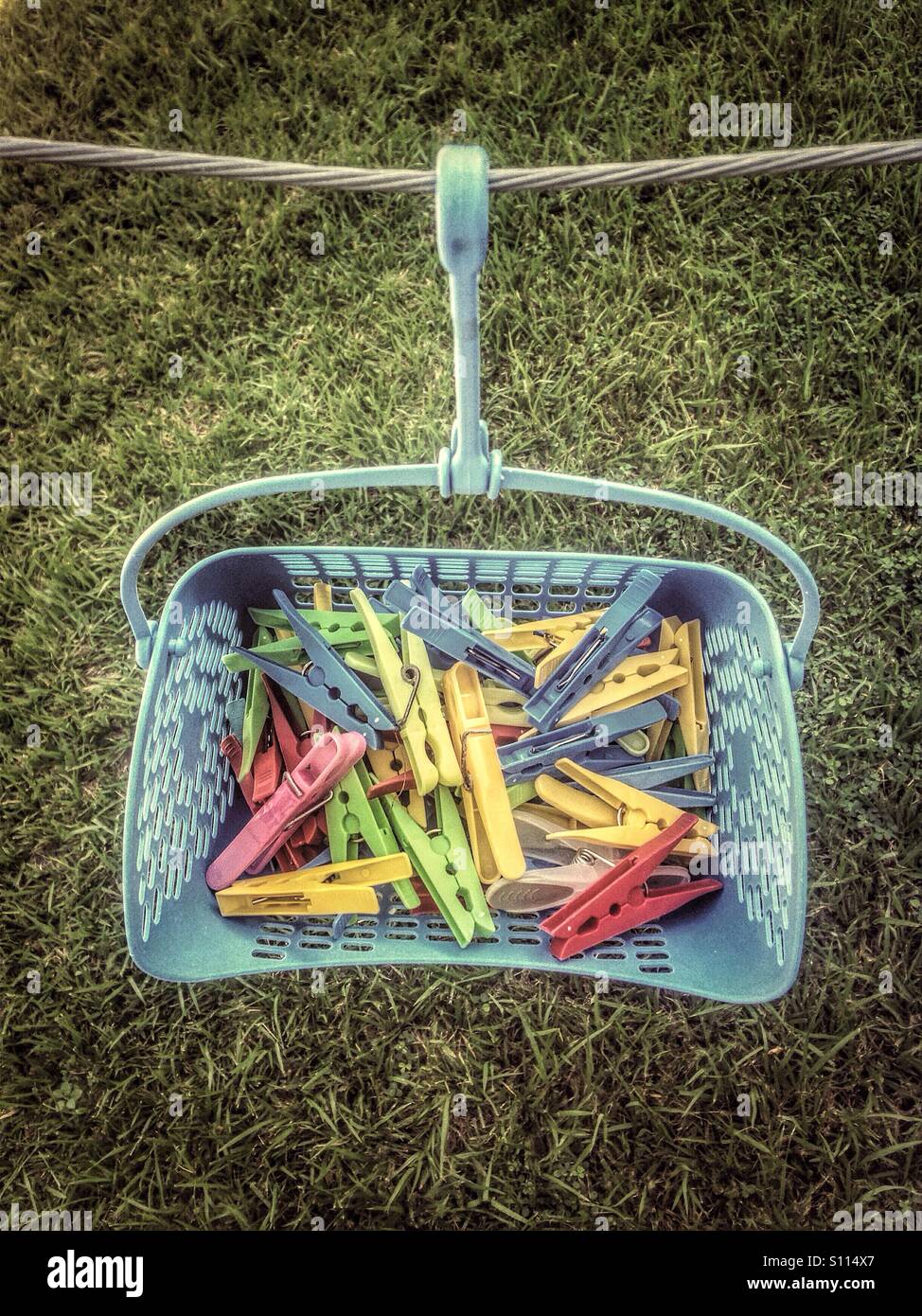 Plastic clothes pegs in a basket suspended to a clothes line. Stock Photo
