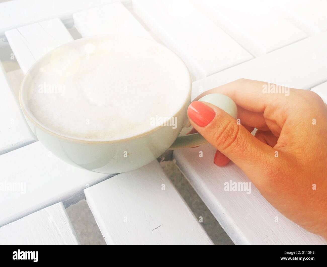 A closeup of a woman's hand holding onto a cup of cappuccino outdoors. - Smartphone Captured Stock Image