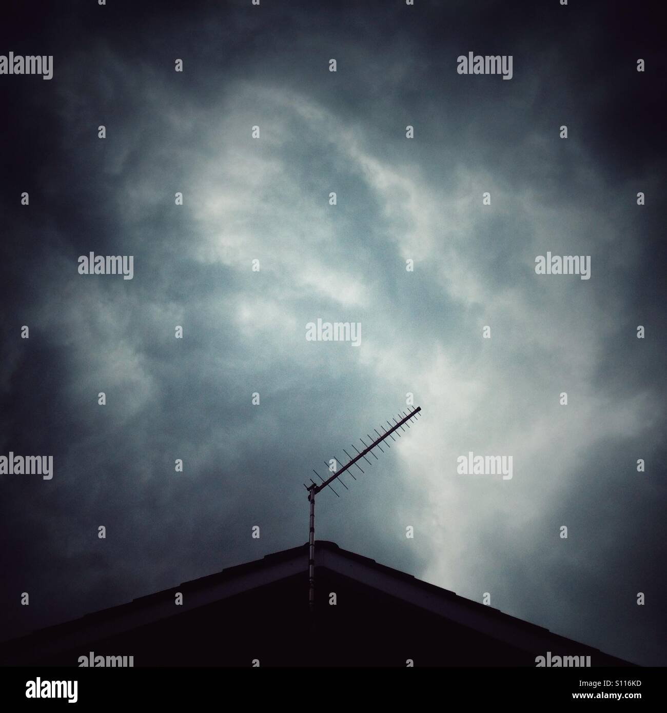 Dark clouds over a roof top of a house with a TV aerial. Stock Photo