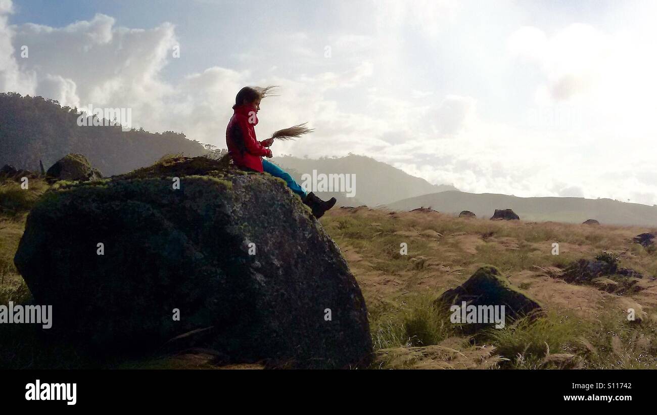 Young girl sitting on a rock in a windy mountain field Stock Photo