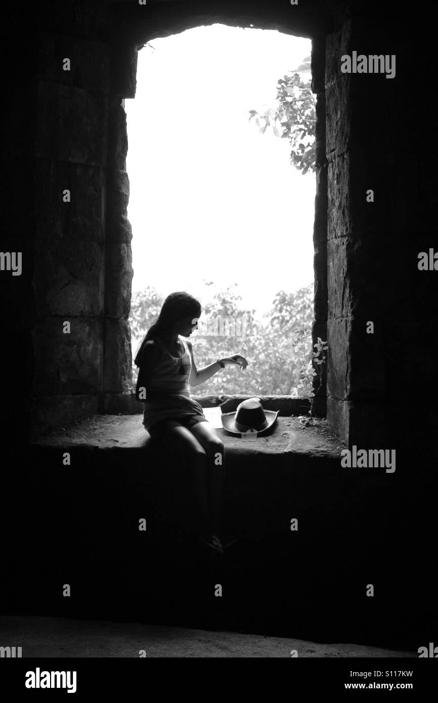 Silhouette of a young girl sitting in a window of the Spanish colonial ruins of Ft. San  Lorenzo in the republic of Panama. Stock Photo