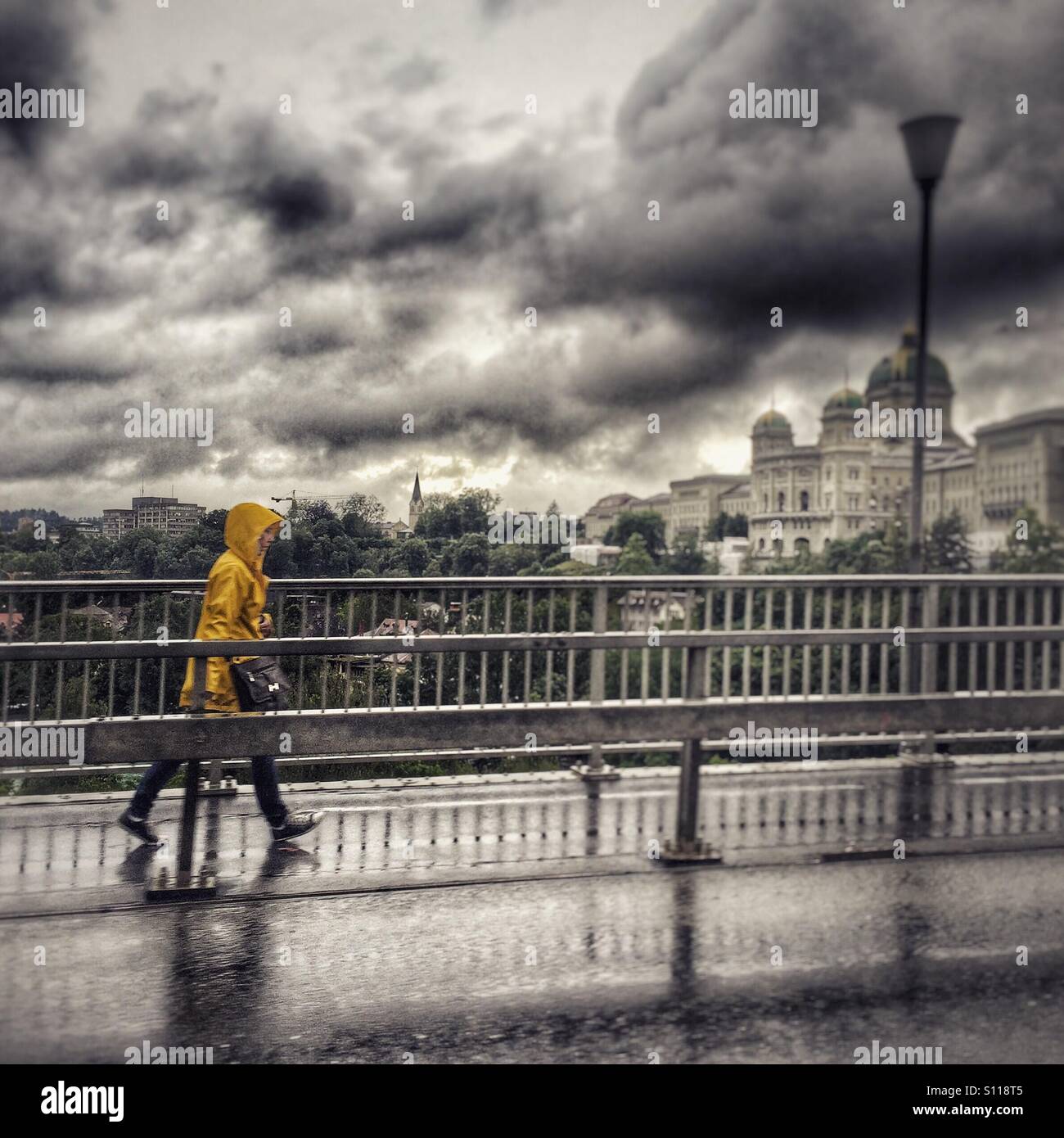 Pedestrian in yellow raincoat hurries across a bridge in Berne, Switzerland, with Swiss parliament in background - Smartphone Captured Stock Image