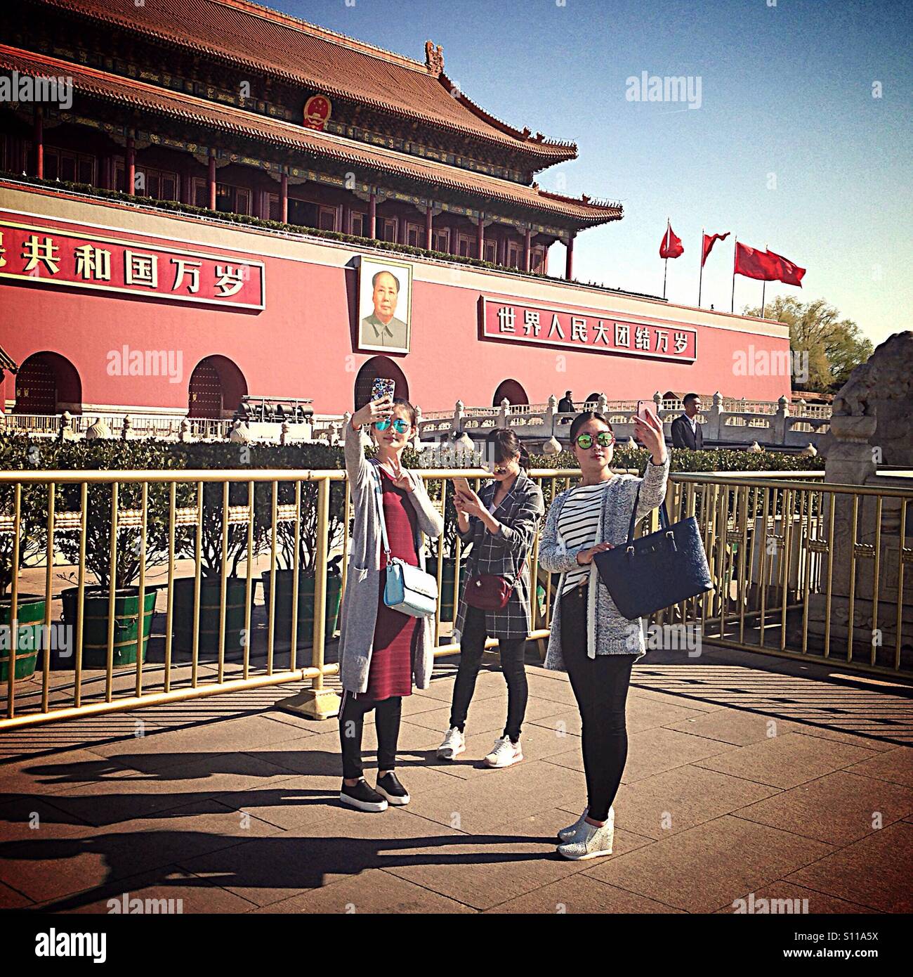 Chinese girls making selfies in front of Mao Zedong's portrait in Forbidden City in Beijing - Smartphone Captured Stock Image
