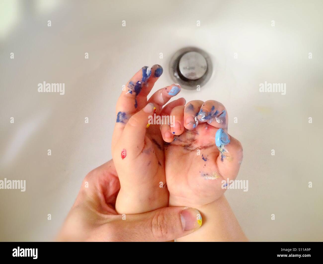 Adult hand whasing painted baby hands in the sink Stock Photo