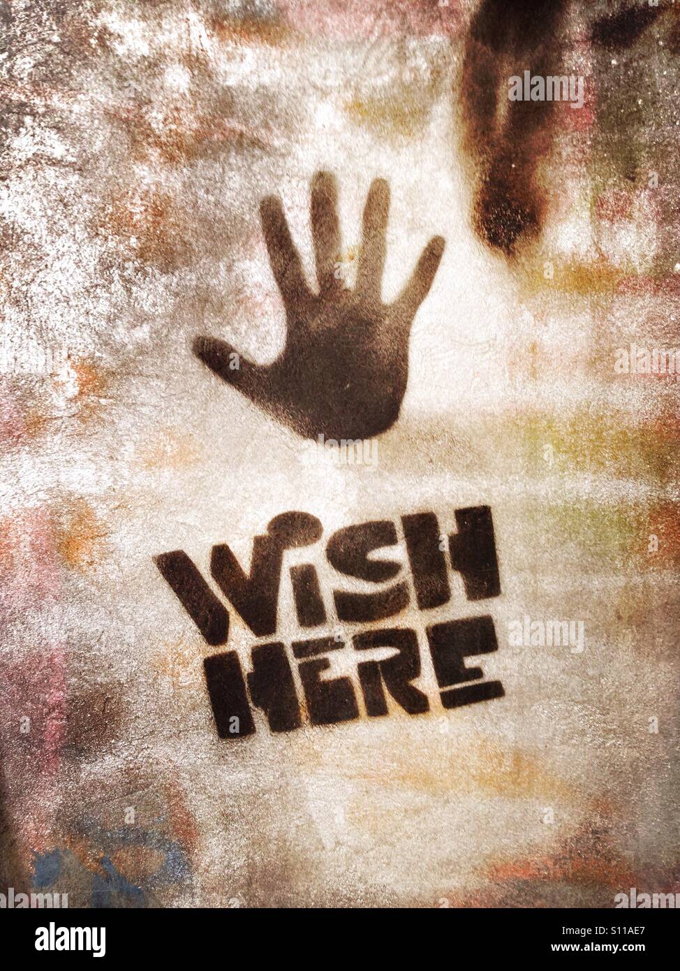A humorous stencil graffiti on a wall in the Berlin district Kreuzberg saying wish here and showing a hand print - Smartphone Captured Stock Image