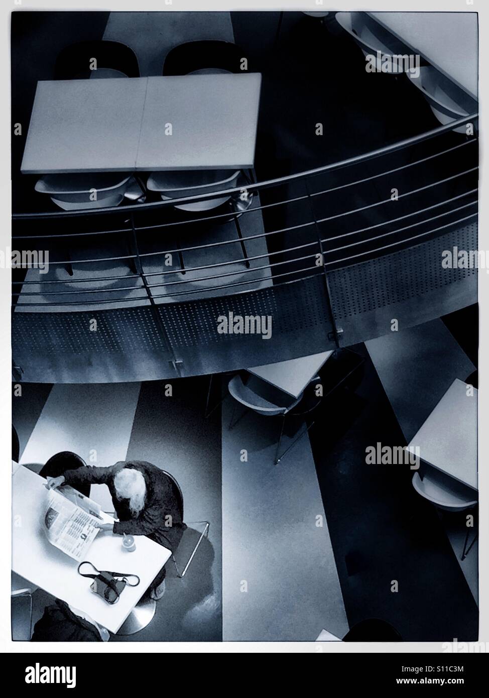 Lonely person ready a newspaper in an empty shopping mall dining area. - Smartphone Captured Stock Image