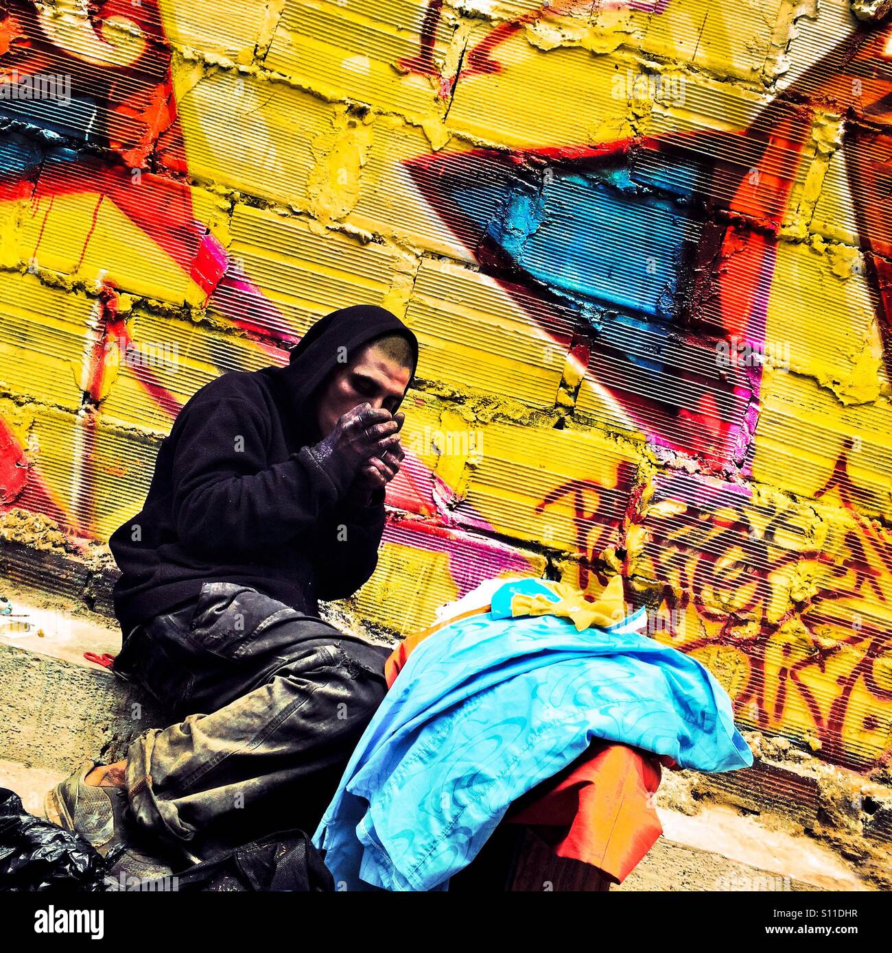 A Colombian drug addict smokes ‘basuco’ (raw cocaine paste) in front the wall, covered in graffiti artwork in the center of Bogotá, Colombia, 15 February, 2016. Stock Photo