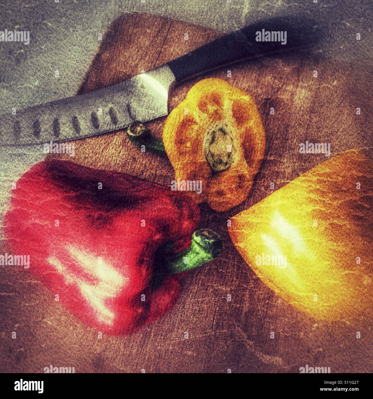 Stylised still life of red and yellow bell peppers with a chef’s knife on a wooden board, evoking seasonal cooking, quality ingredients and calm kitch - Smartphone Captured Stock Image