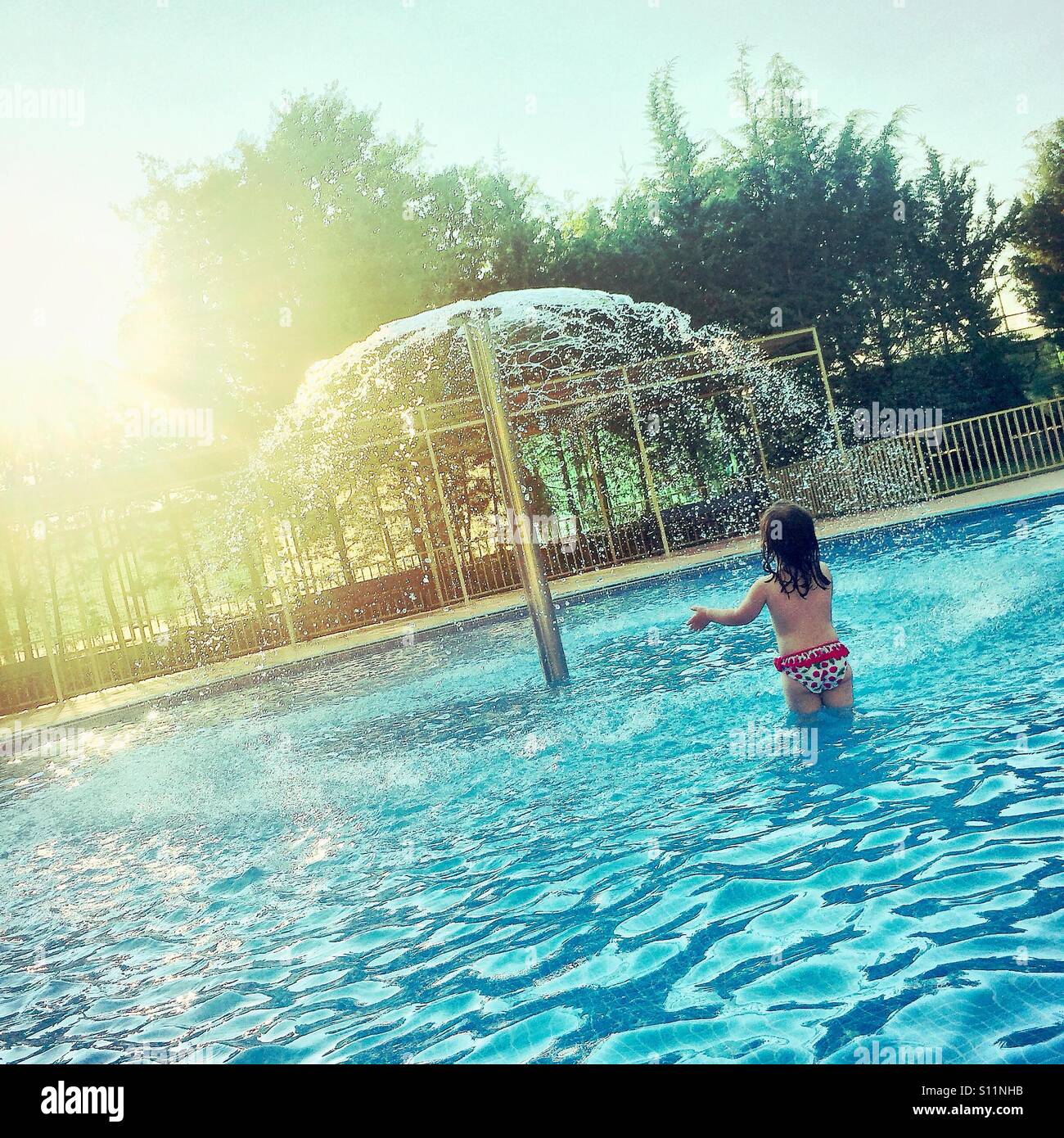 Little two year old girl playing in a swimming pool with fountain at