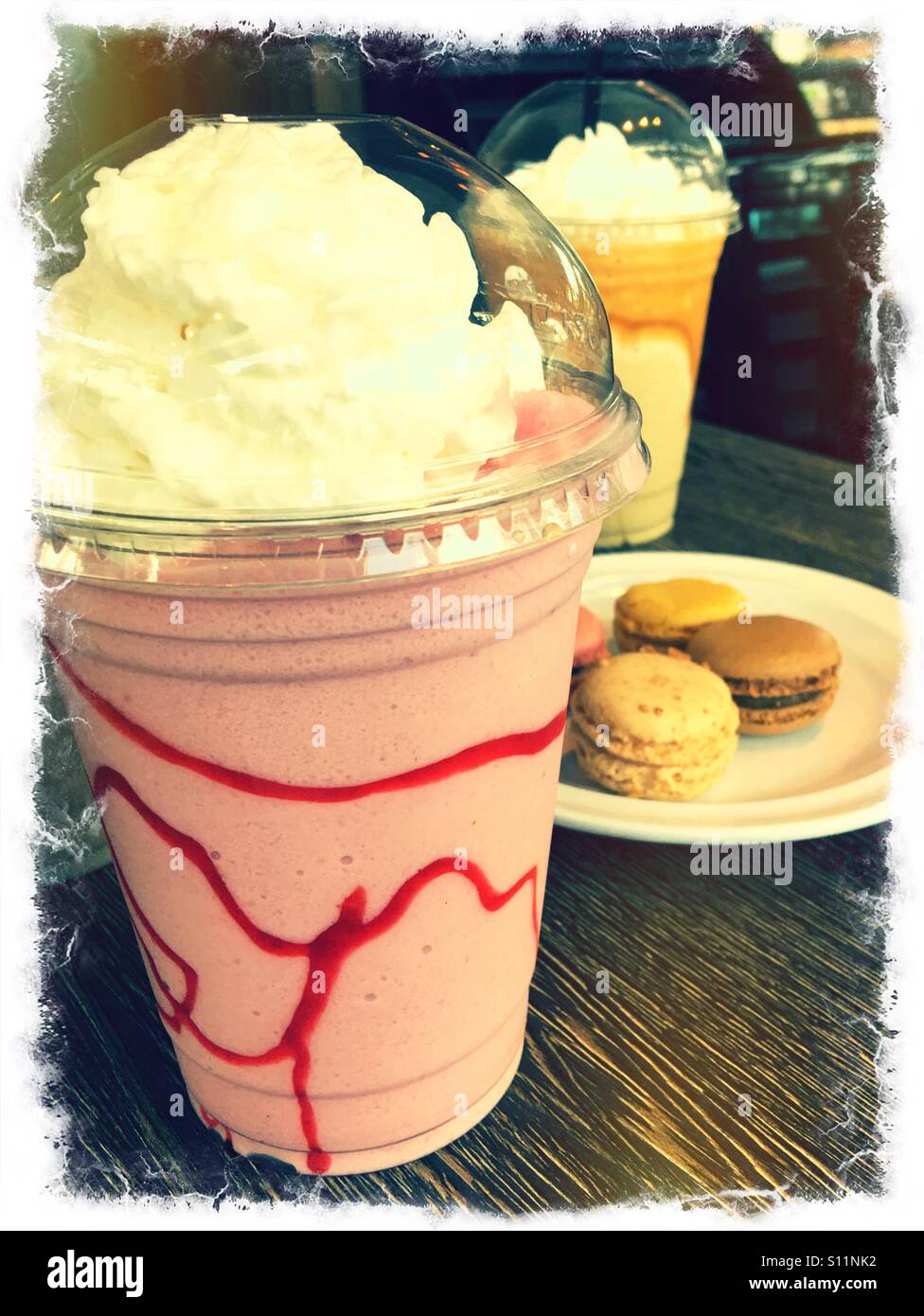 A strawberry frappe with French macarons and a caramel frappe in the background. Stock Photo