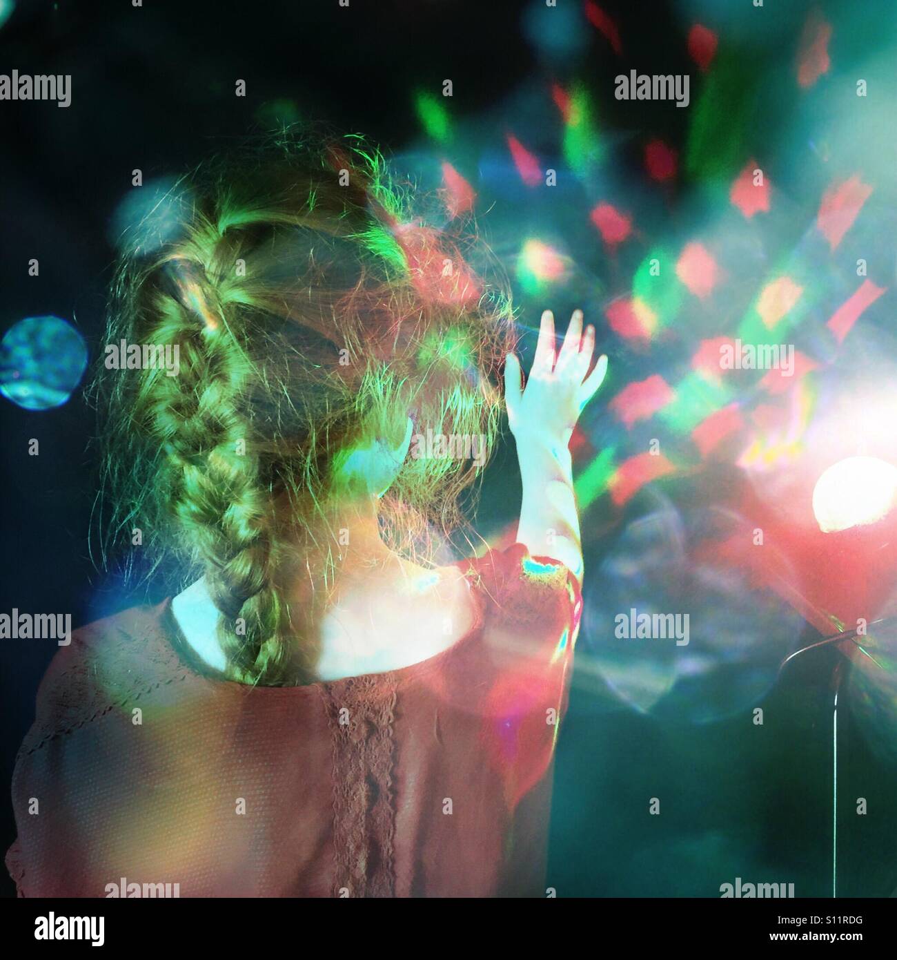Young girl reaches out to coloured lights Stock Photo