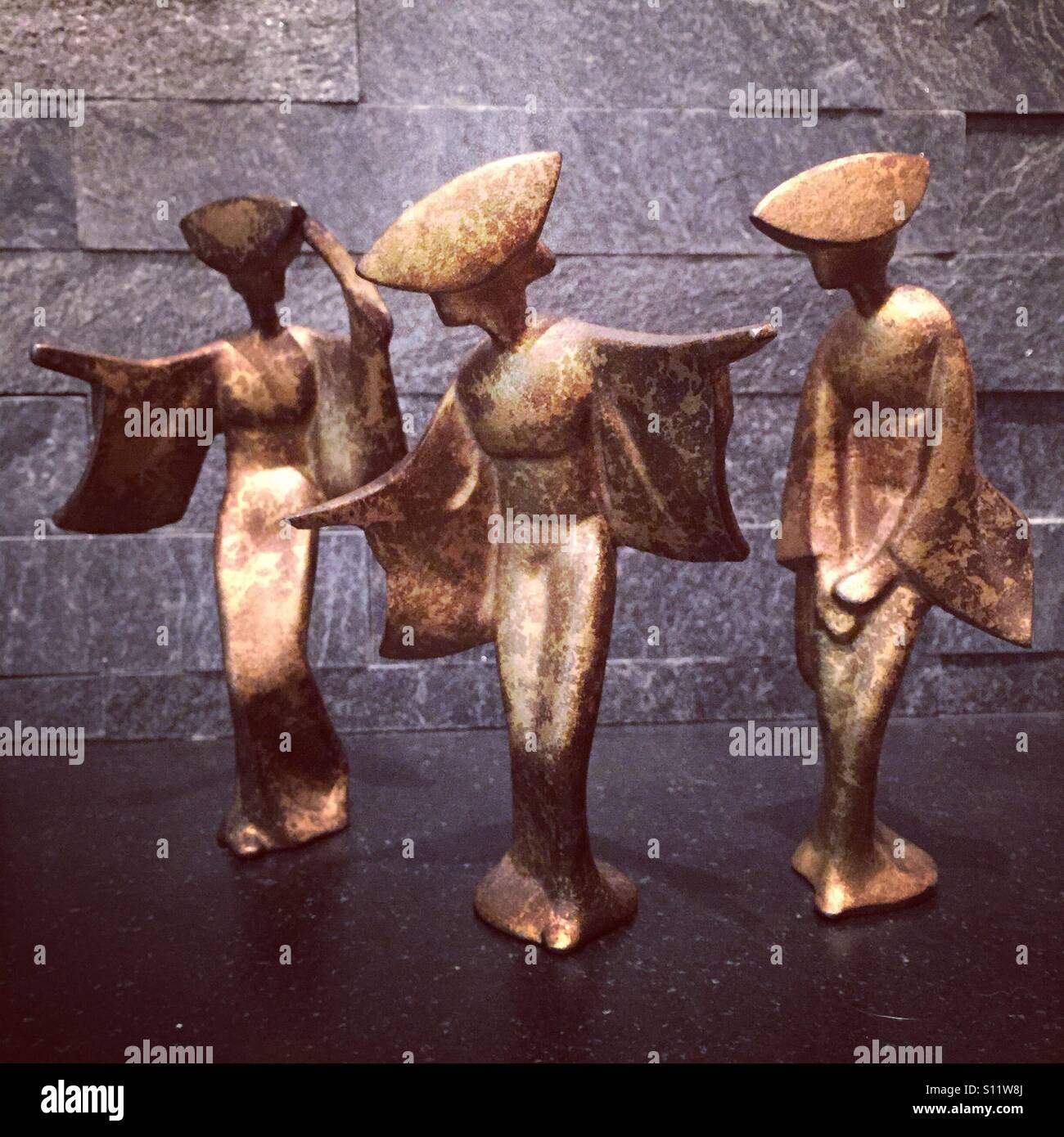 Three vintage golden geisha girl statues pose gracefully. - Smartphone Captured Stock Image