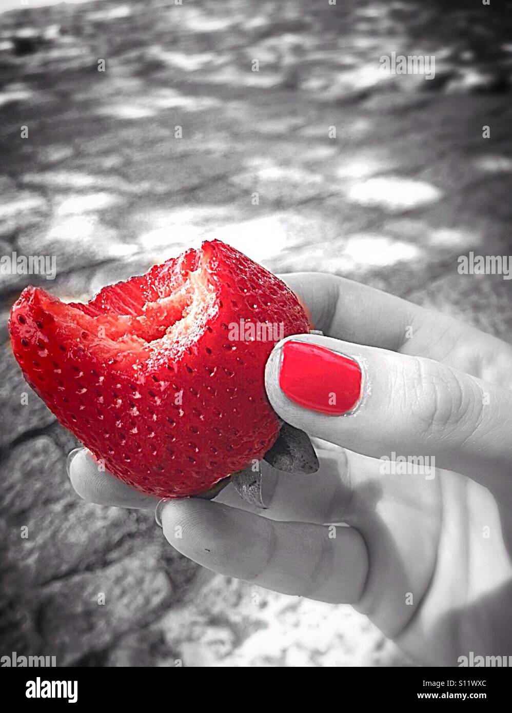 Bitten strawberry in hand. Red color combined with black and white - Smartphone Captured Stock Image