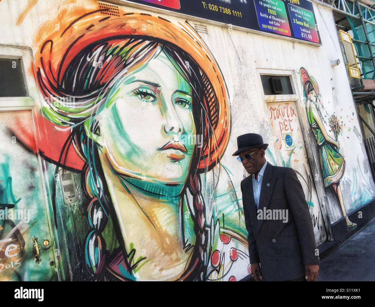 Pedestrian passing by a brightly painted mural of a woman's face in Camden Town, London, U.K. Stock Photo