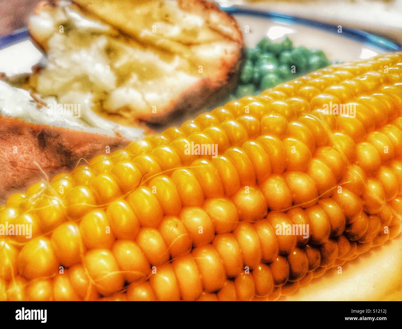 Corn on the cob, baked potato with cheese and butter, and fresh green peas. An unbalanced diet. - Smartphone Captured Stock Image