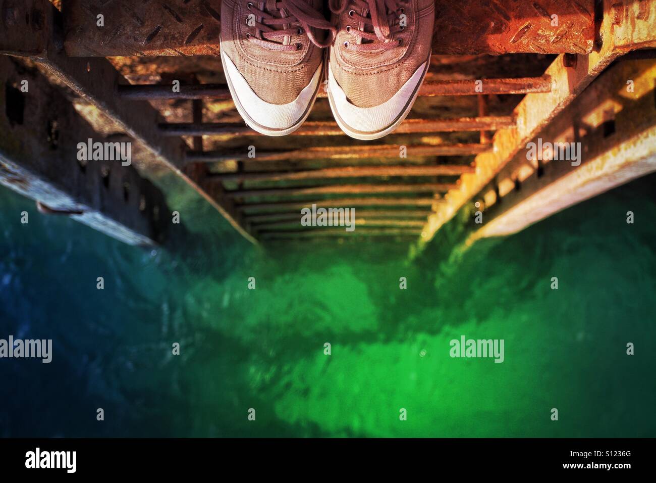 Looking over the precipice into a pool of green toxic liquid. A pair of shoes at the top of a rusty ladder leading down to a green sea. - Smartphone Captured Stock Image