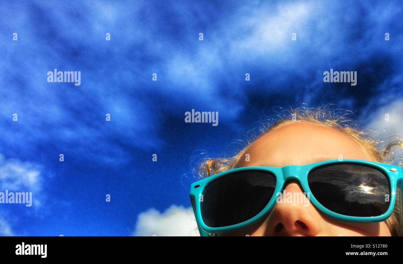 Girl wearing blue framed sunglasses against a blue sky Stock Photo