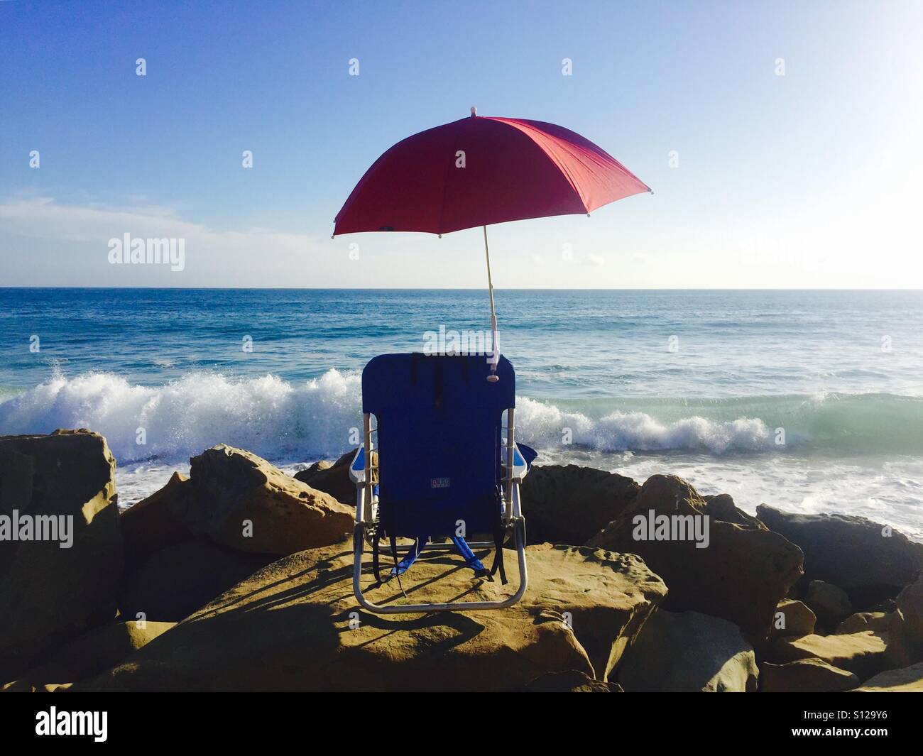 A single red umbrella and a blue chair at the beach. Ventura, California USA. Stock Photo