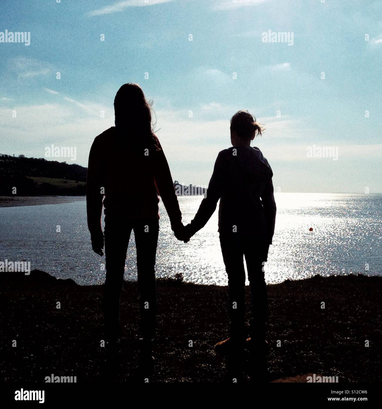 Friends holding hands looking out to sea - Smartphone Captured Stock Image
