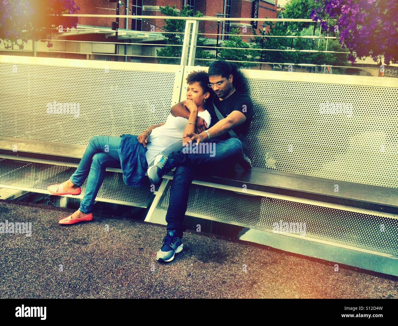 A couple sit together outside on a bench. - Smartphone Captured Stock Image