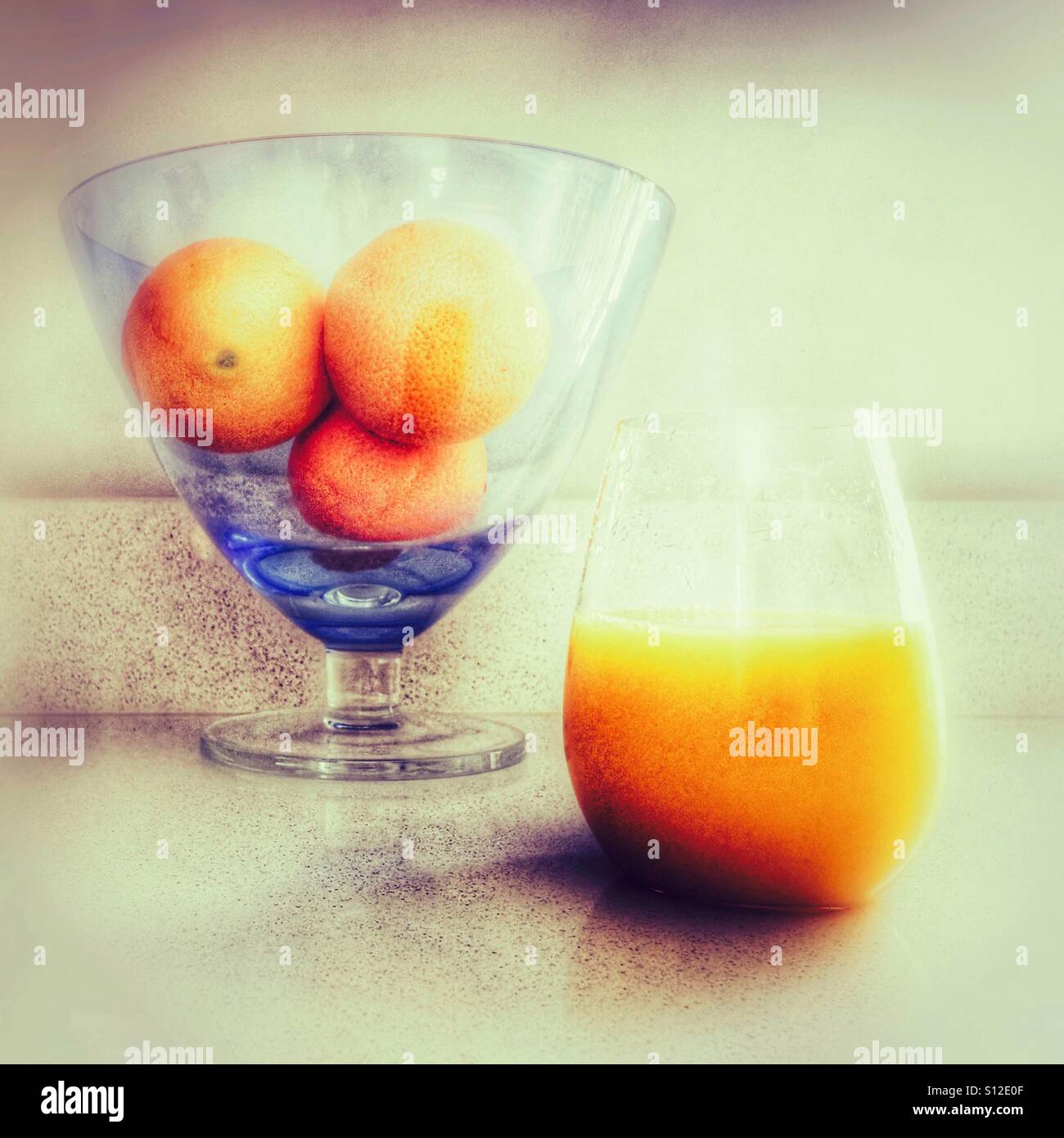 Three oranges in a glass bowl, with a glass of orange juice alongside. Stock Photo