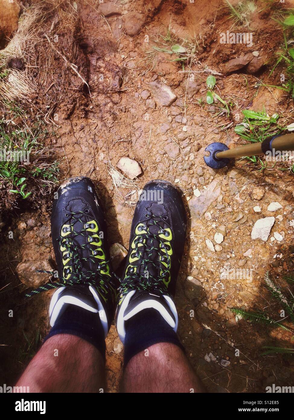 A pair of hiking boots and male legs on the loamy ground of a trail in the Alps Stock Photo