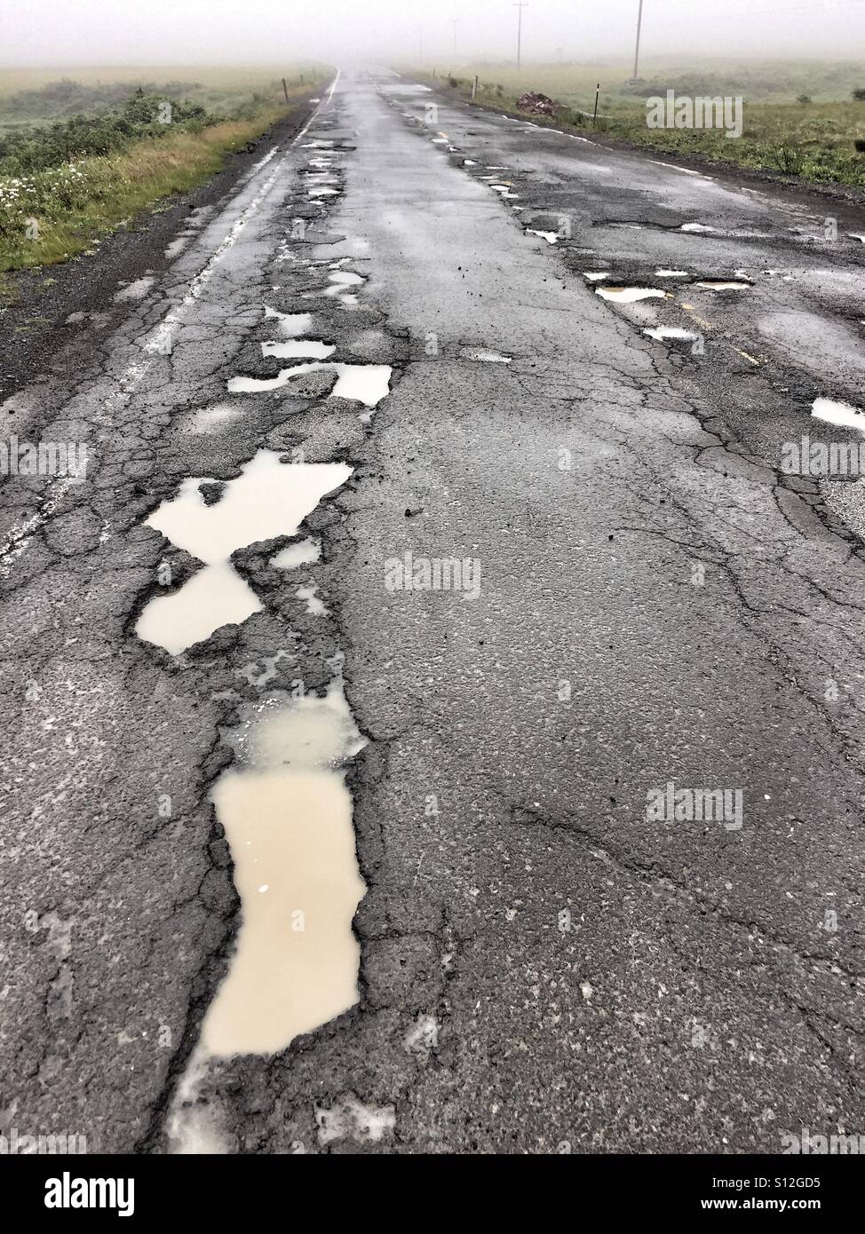 Potholes filled with muddy water on a lesser-used highway. Stock Photo