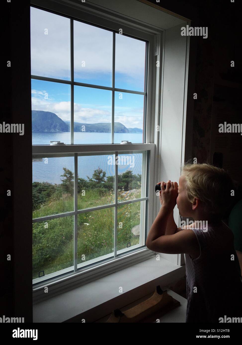 A girl surveys the coast with a spotting scope through a window. - Smartphone Captured Stock Image