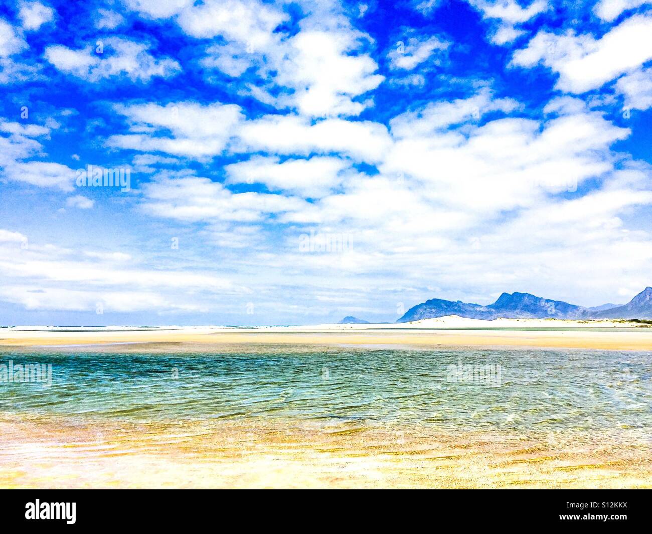 Deep blue sky with puffy clouds over shallow lagoon and sand dunes. Stock Photo