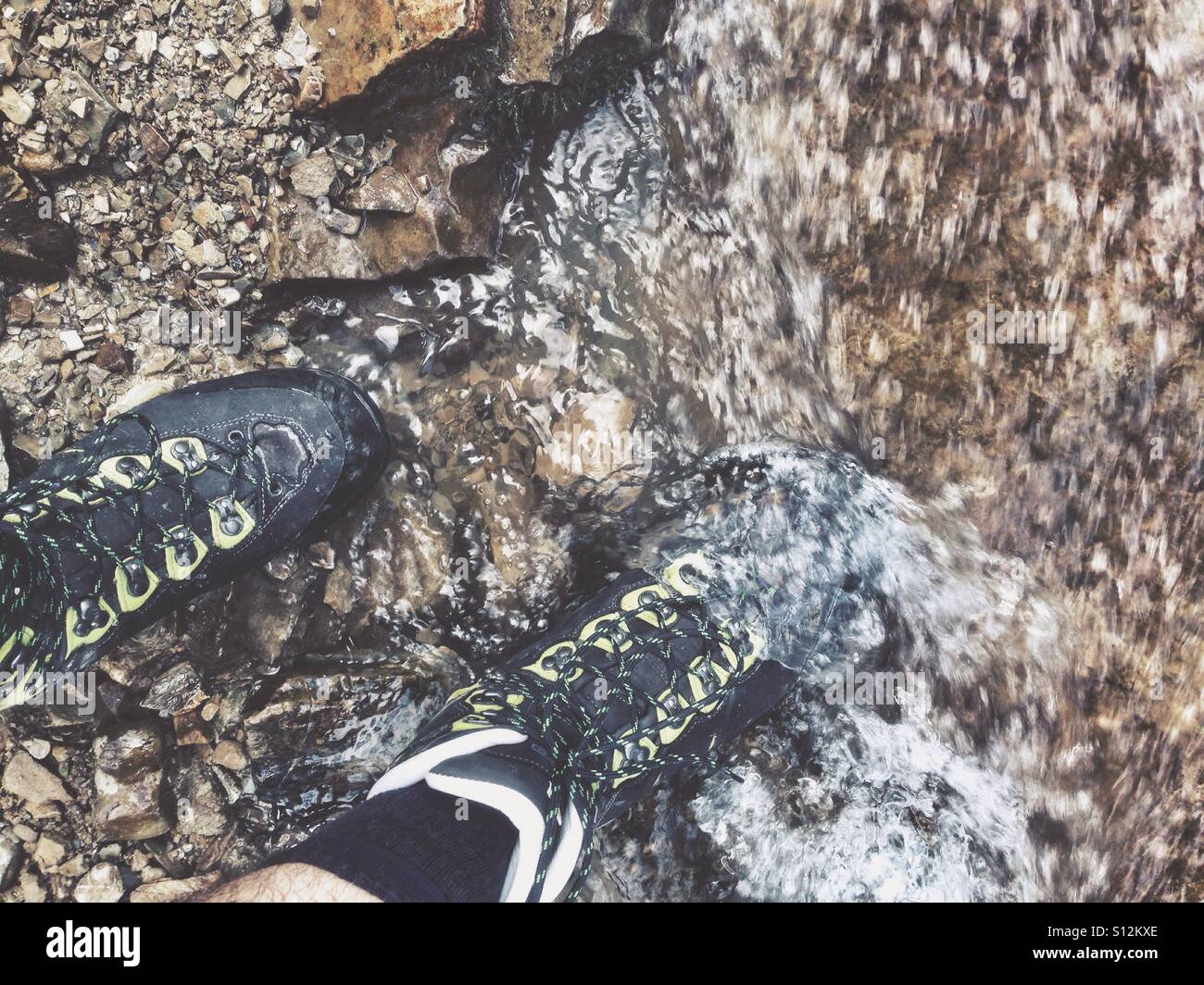 Hiking boots walking into the fresh water of a mountain stream or creek Stock Photo