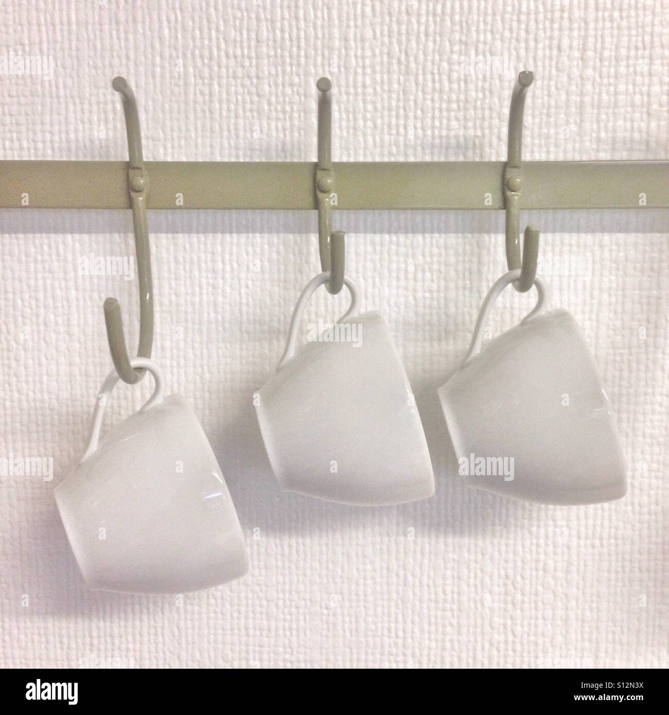 White ceramic cups hanging on hooks against a textured wall showcasing minimalist design - Smartphone Captured Stock Image