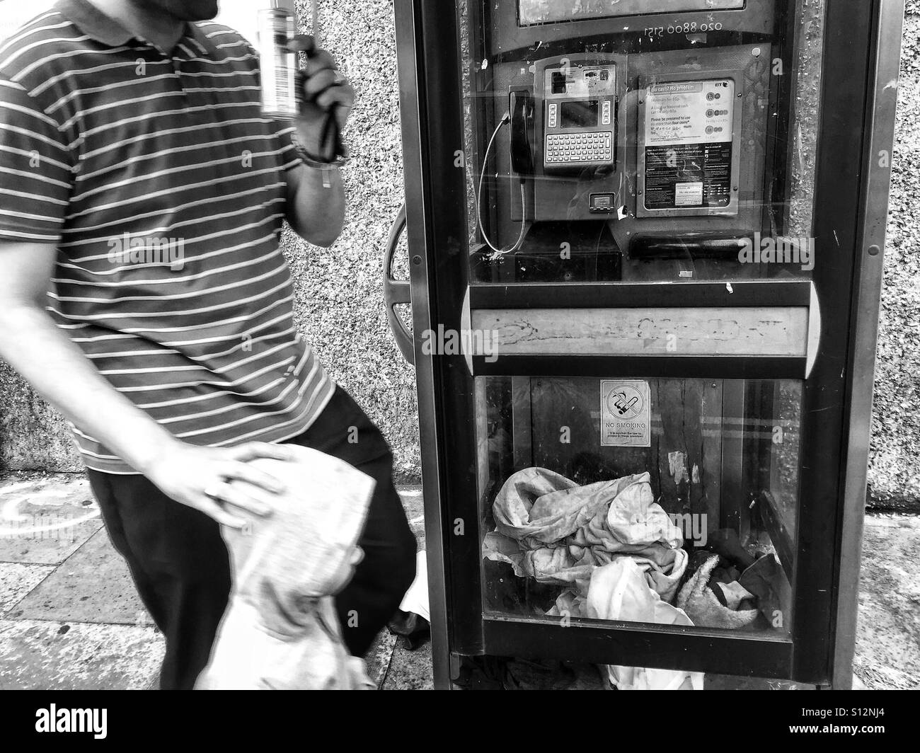 Man walking by a phone box, full of a homeless persons bedding. London